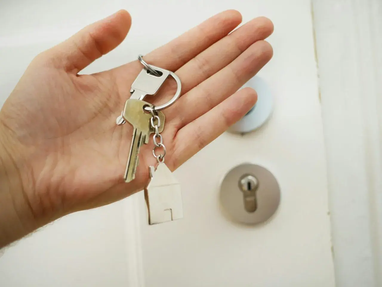 En hand håller nycklar med ett hus som berlock. Dags att byta lås och få nya nycklar till hemmet.
