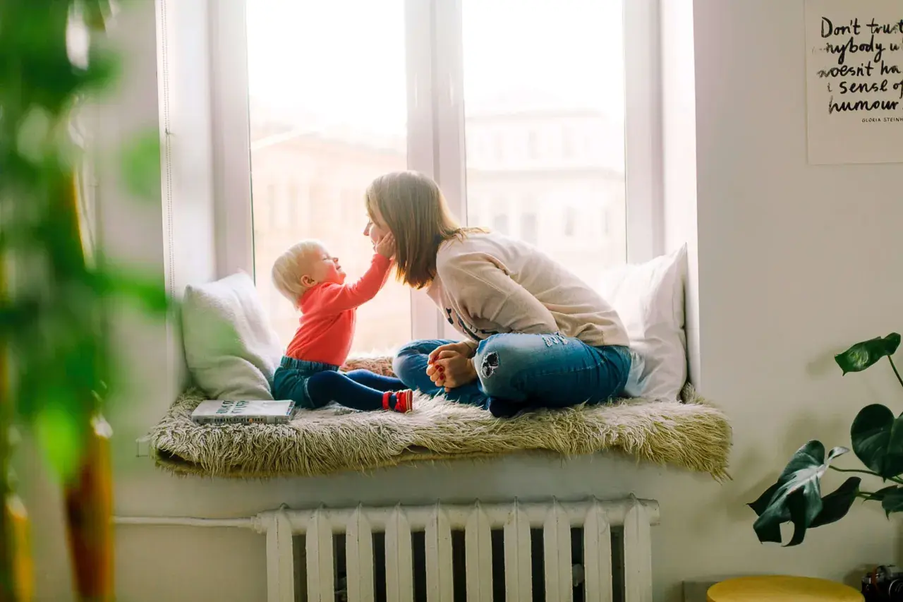 Mama i dziecko siedzą na parapecie. Wzór umowy najmu mieszkania dla rodziny z dzieckiem jest na książce.