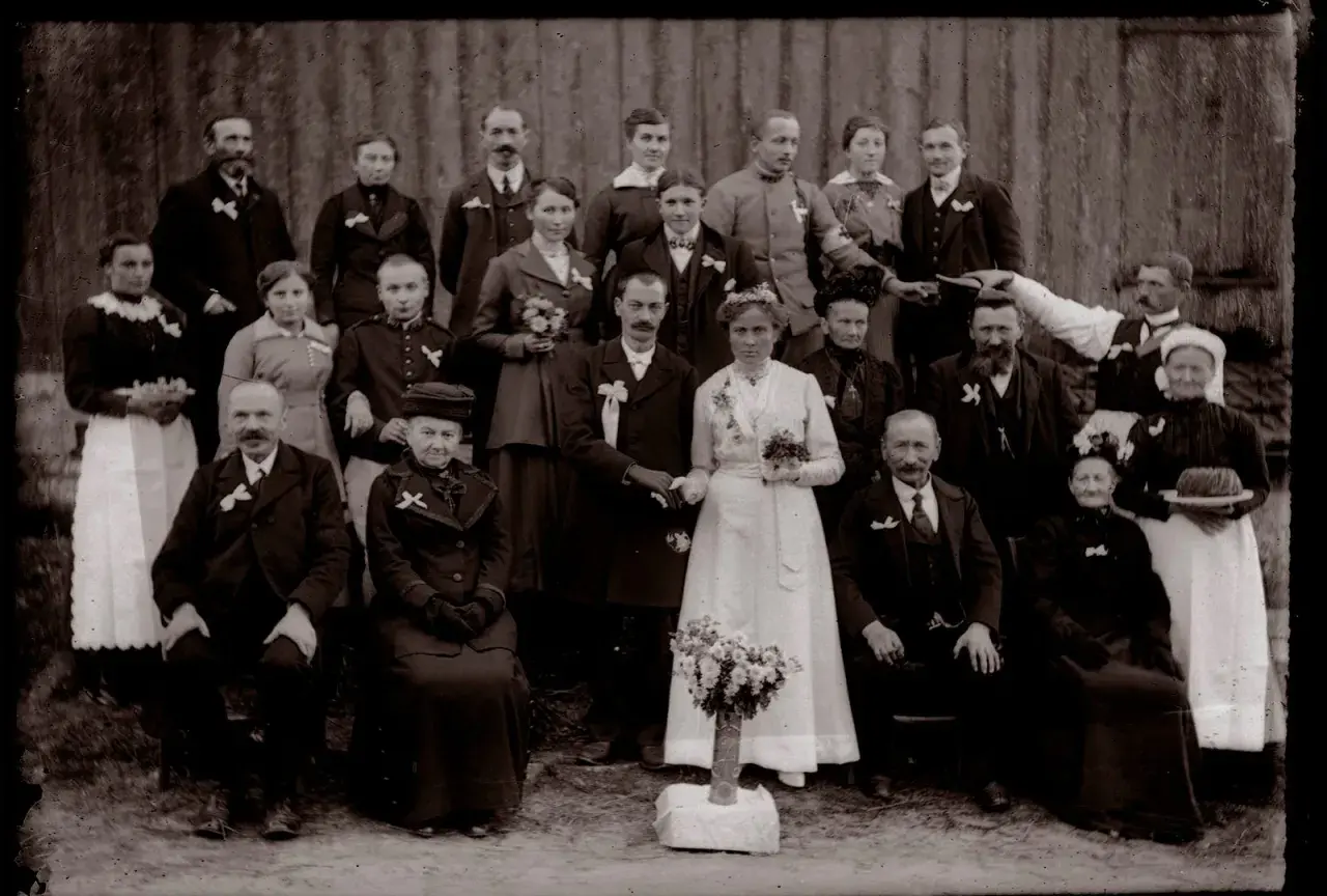 Un groupe de familles posant pour un recensement ad 88. La mariée, en blanc, tient un bouquet.