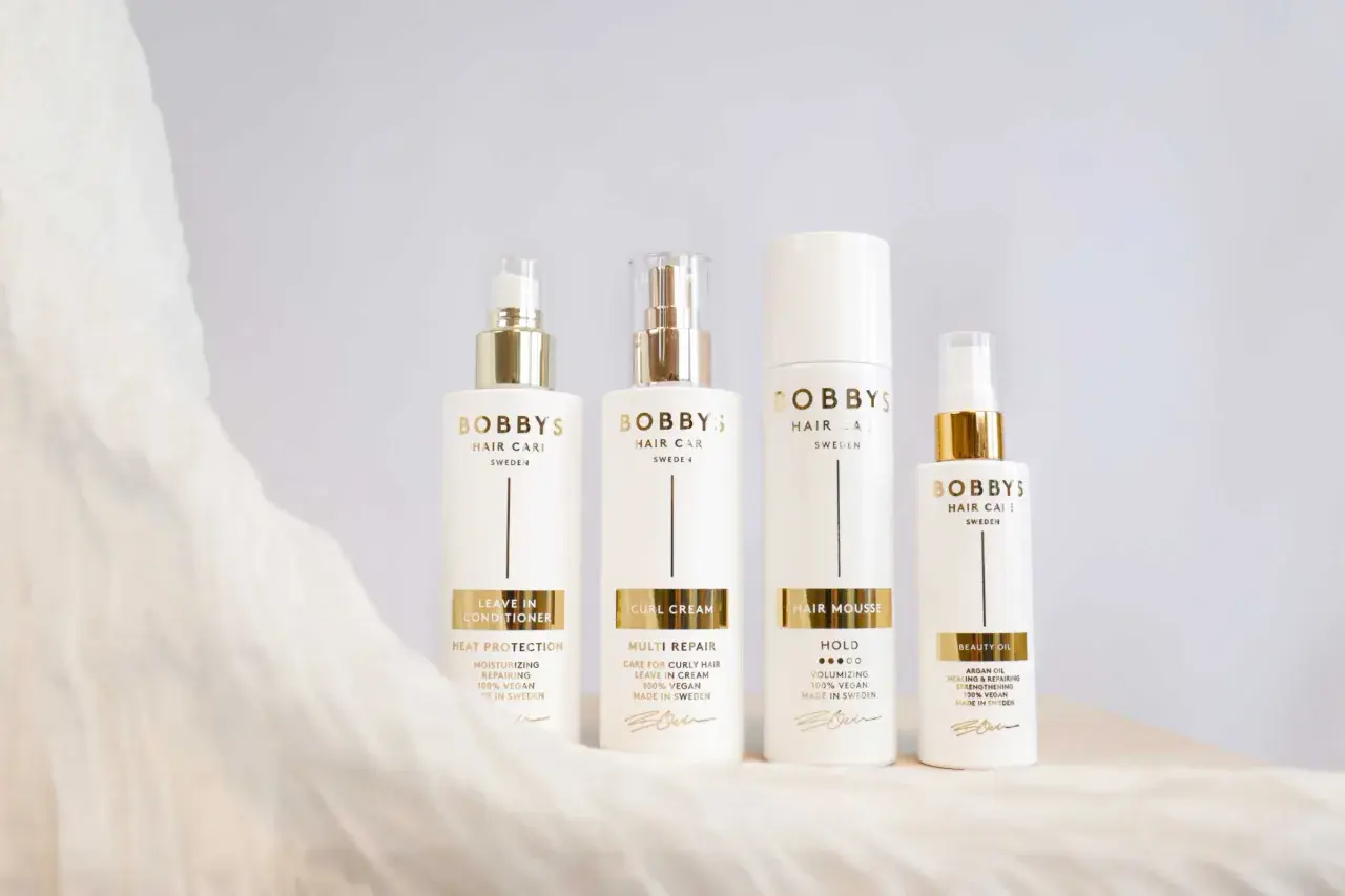 Fyra vita flaskor med guldfärgade detaljer från Bobby's Hair Care. En huskur mot statiskt hår.