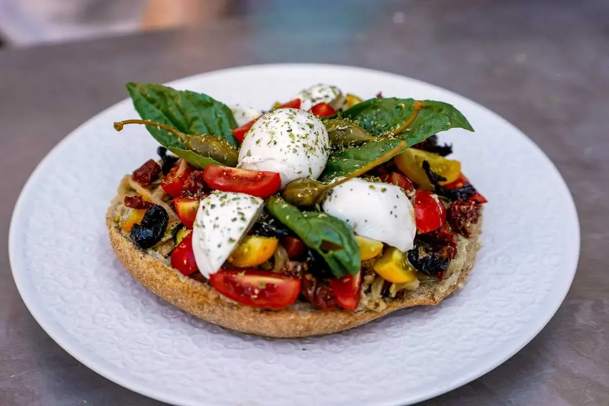 Frisches Brot belegt mit Tomaten, Kapern, Oliven und verschiedenen Mozzarella Arten, garniert mit Basilikum.