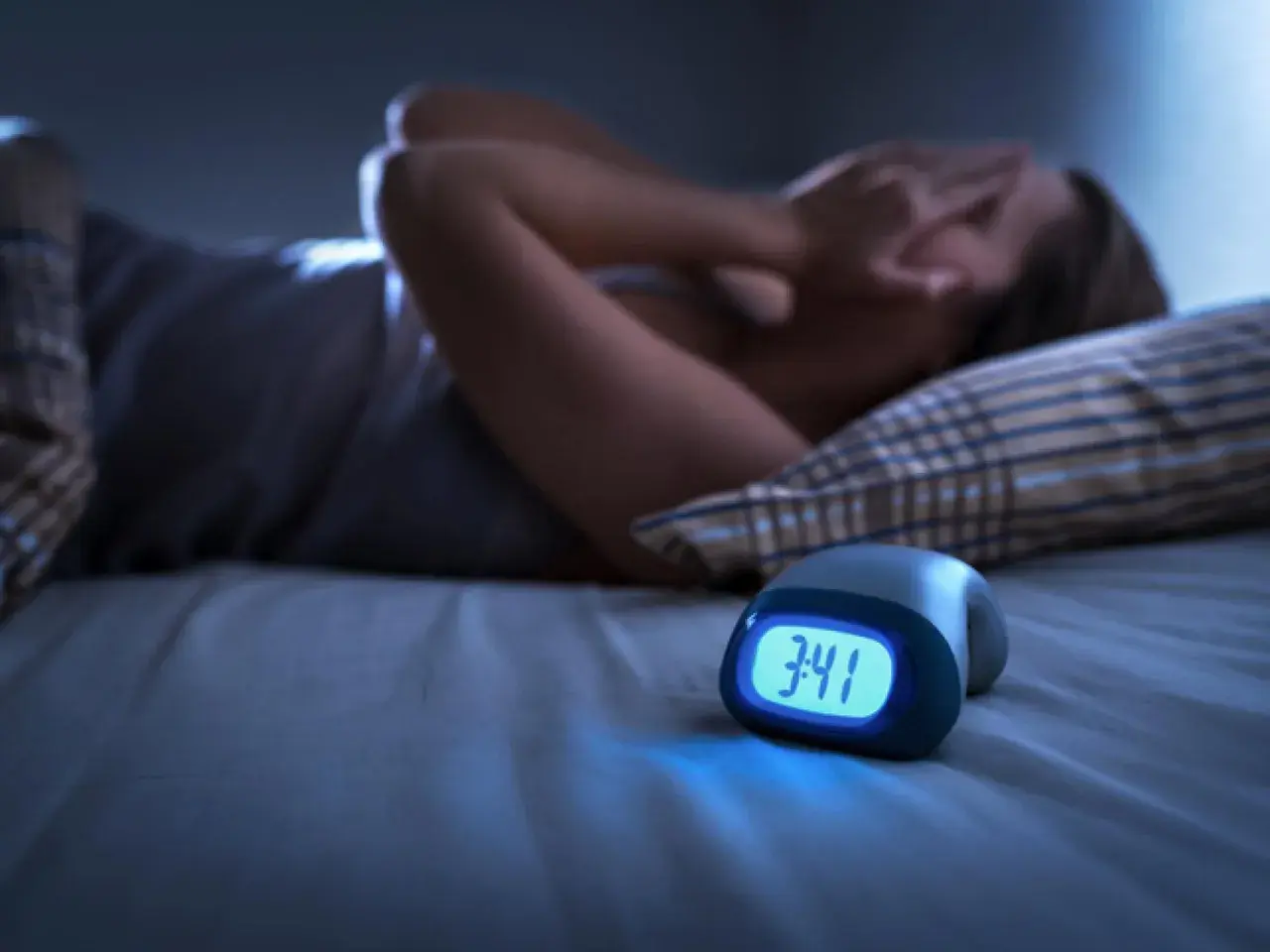 Persona en la cama, cubriéndose la cara, con un despertador marcando las 3:41. Parece que está teniendo una pesadilla, como si soñara que te persiguen para matarte.