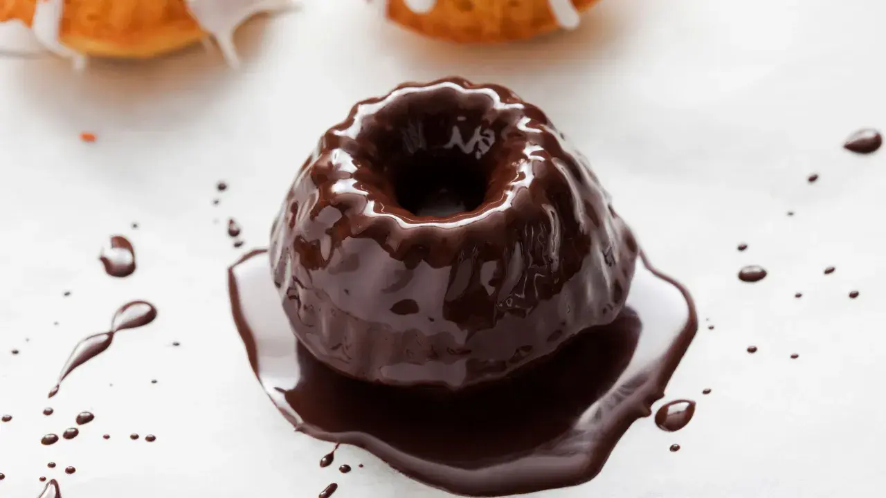 Una torta con glassa al cioccolato, lucida e invitante, con gocce di cioccolato che si spargono sul bianco.