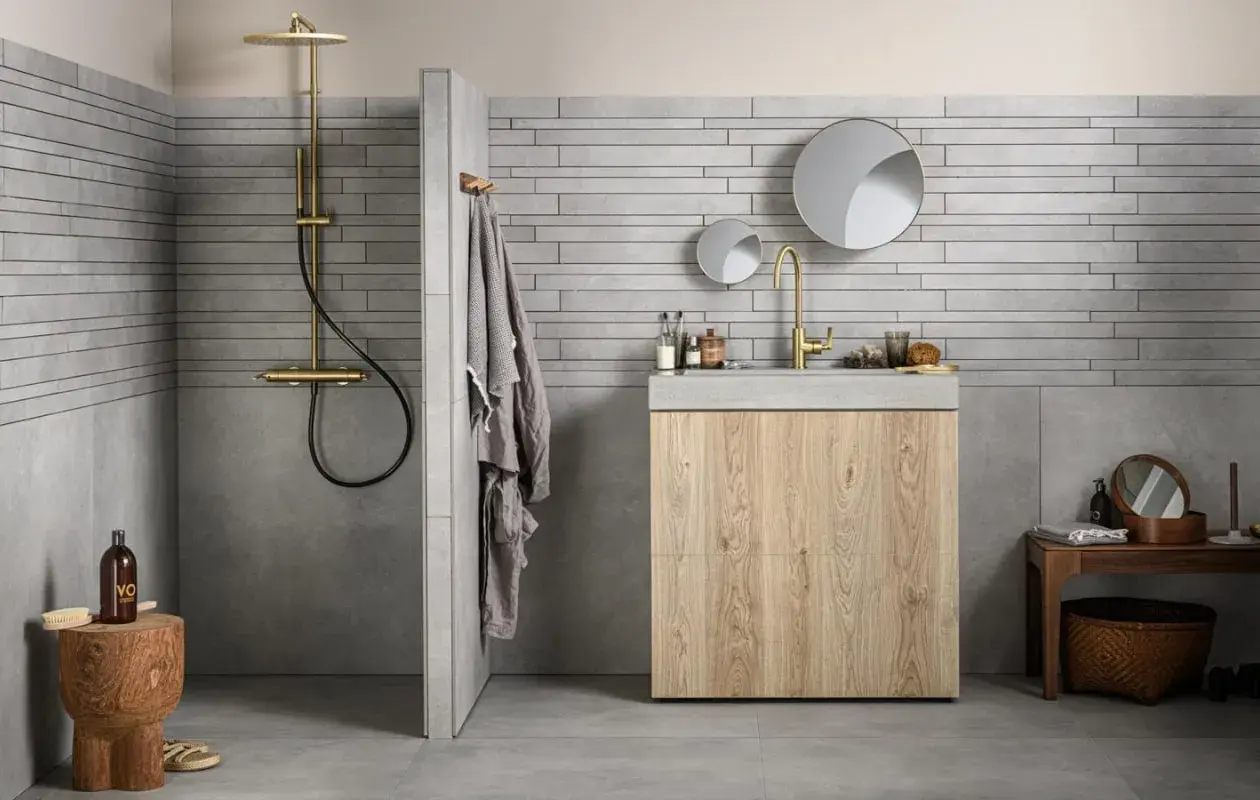 Grijze badkamer met houten meubel. Welke kleur handdoeken passen hierbij? Een grijze handdoek hangt aan de muur.