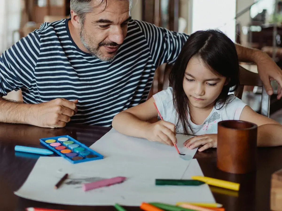 Padre e hija pintando con acuarelas y lápices de colores. Un momento de creatividad con materiales de escuela infantil.