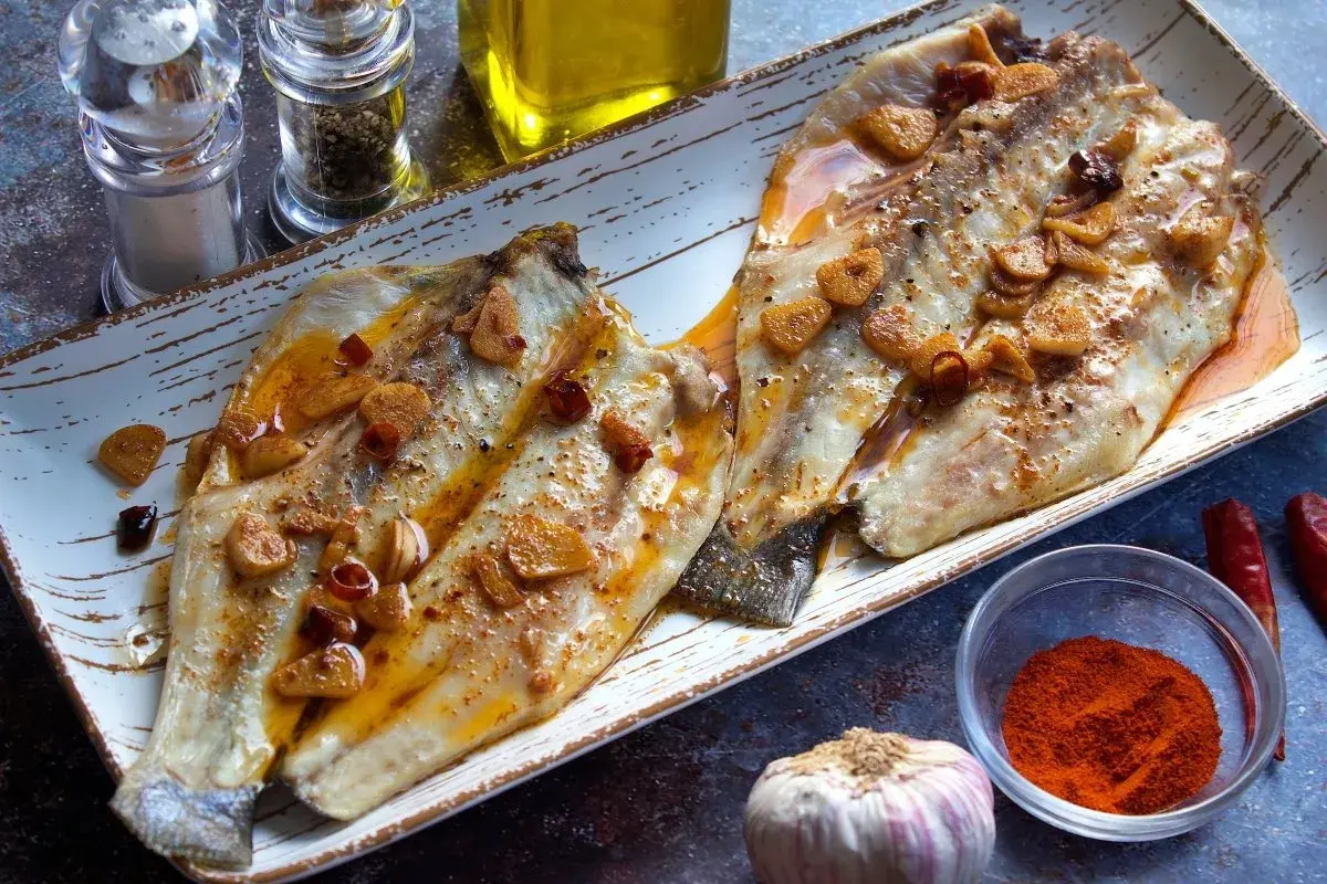 Dos filetes de lubina a la bilbaina, dorados y jugosos, con láminas de ajo y guindilla, listos para disfrutar.
