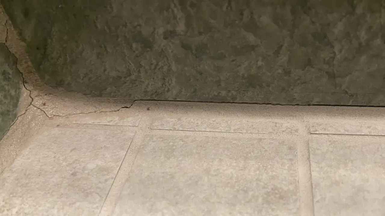 Pęknięta, biała masa między płytkami sugeruje, że szukamy co zamiast fugi. Zielona ściana nad nią.