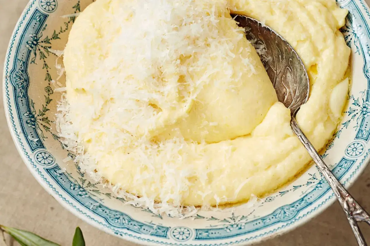Cremige Polenta, frisch gekocht und mit Parmesan bestreut, wartet in einer blumig verzierten Schüssel auf den Löffel.