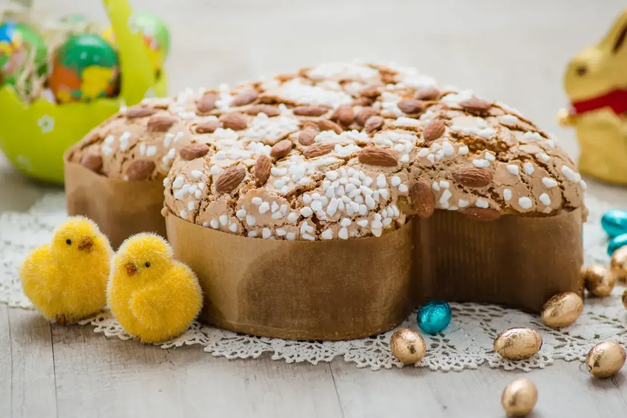 Colomba pasquale, un classico tra i dessert pasquali, decorata con mandorle e zuccherini, circondata da pulcini e uova di cioccolato.