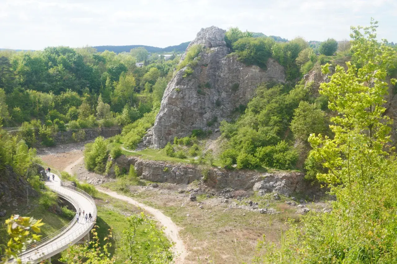 Kamieniołom w Kielcach z krętą ścieżką i grupą spacerowiczów. W oddali skaliste góry porośnięte zielenią.