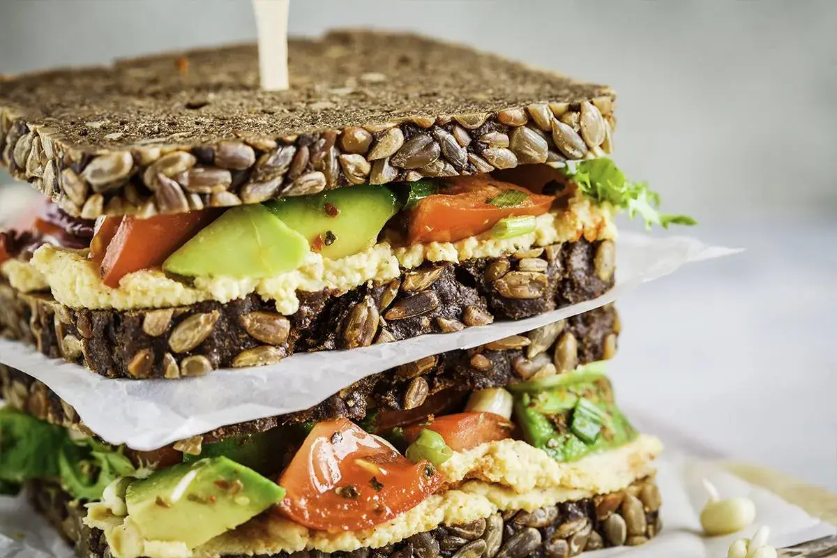 Delicioso sandwich de hummus con aguacate, tomate y pan integral con semillas.