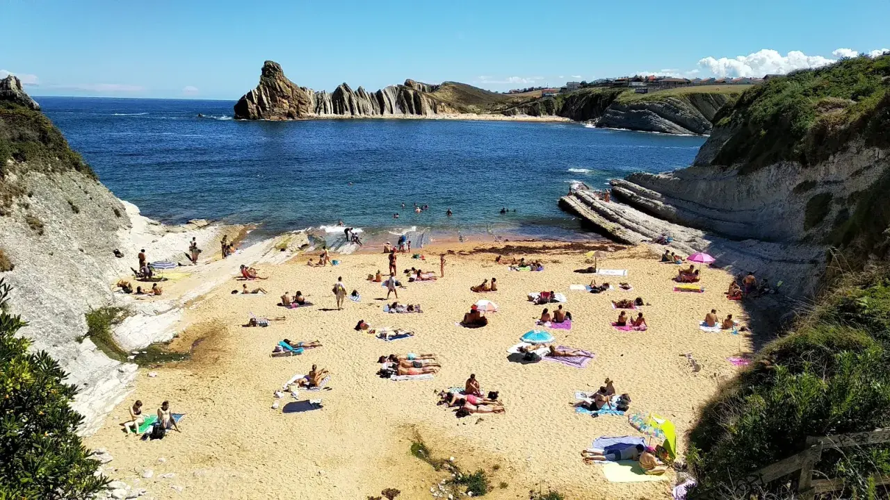 Gente disfrutando del sol y el mar en la playa de cerrias, con formaciones rocosas impresionantes.