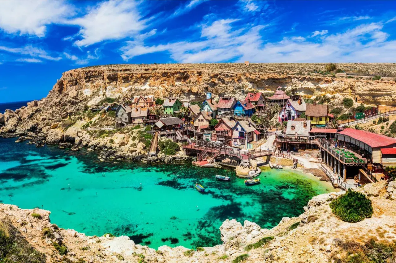 Bunte Häuser am malta beach, umgeben von Felsen und türkisfarbenem Wasser. Boote schaukeln sanft in der Bucht.