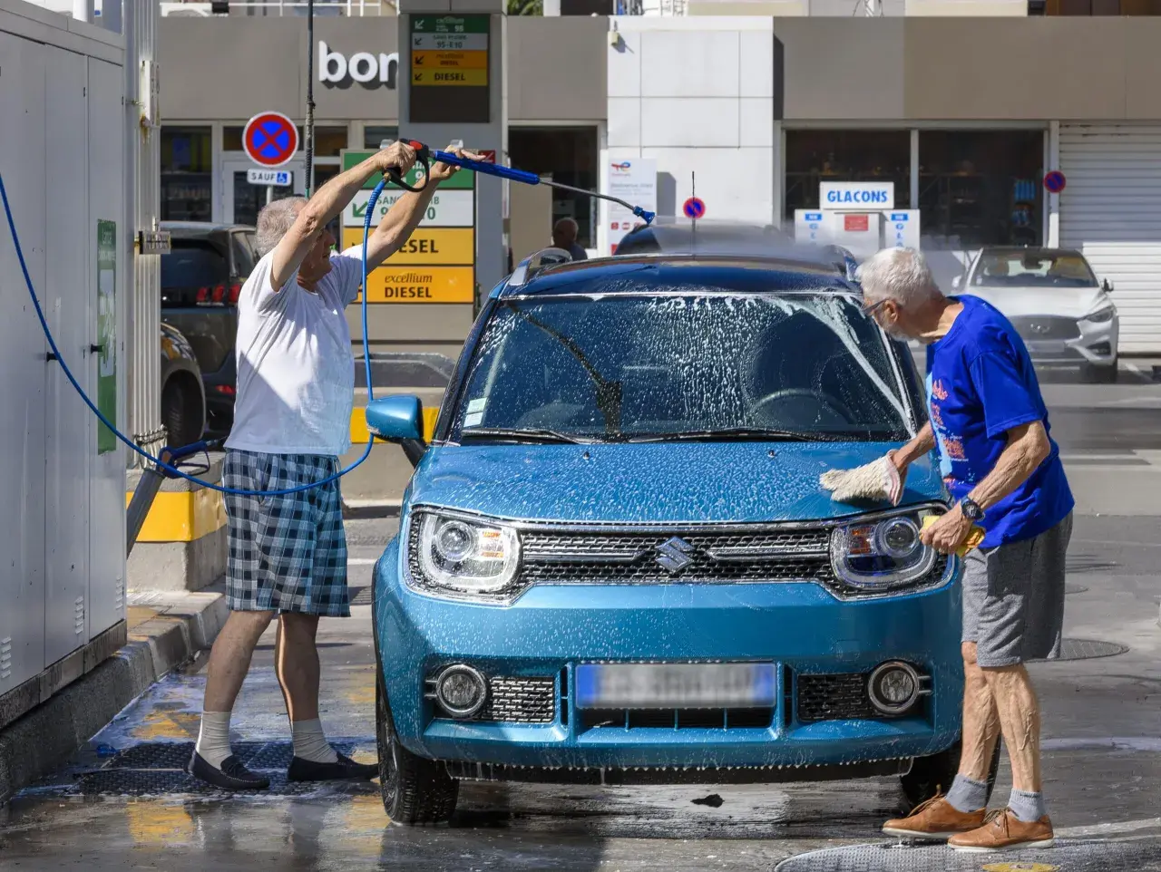 Deux hommes lavent une machine bleue avec de la mousse. L'un utilise un nettoyeur haute pression, l'autre frotte avec une éponge.