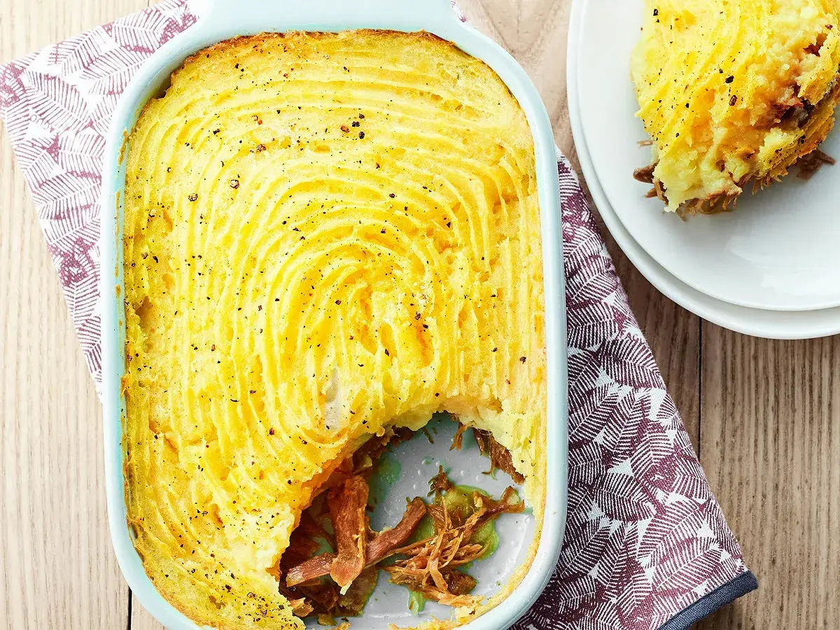 Un parmentier de canard doré et gratiné, prêt à être dégusté. Une portion est servie sur une assiette blanche.