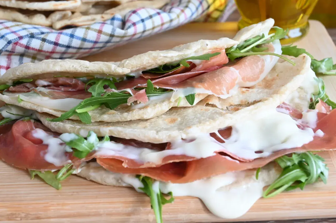 Piadina farcita con prosciutto crudo, mozzarella filante e rucola. Una ricetta piadina veloce e gustosa, perfetta per un pranzo o una cena informale.