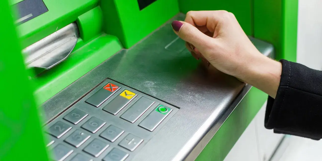 Eine Hand bedient ein grünes Geldautomaten-Bedienfeld. So funktioniert ein Bankwechsel: Geld abheben oder einzahlen.