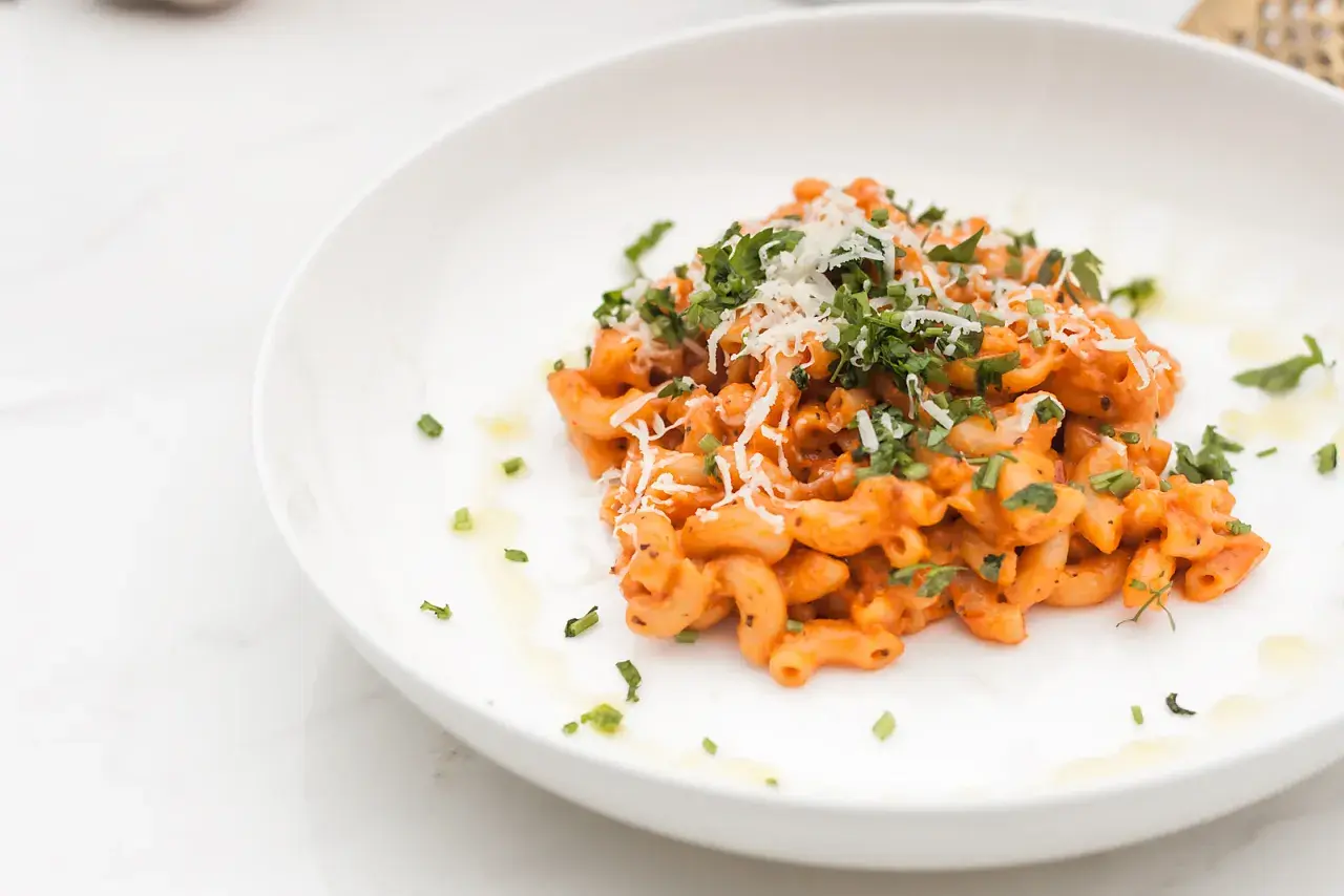 Penne alla vodka z posiekaną natką pietruszki i startym parmezanem na białym talerzu.