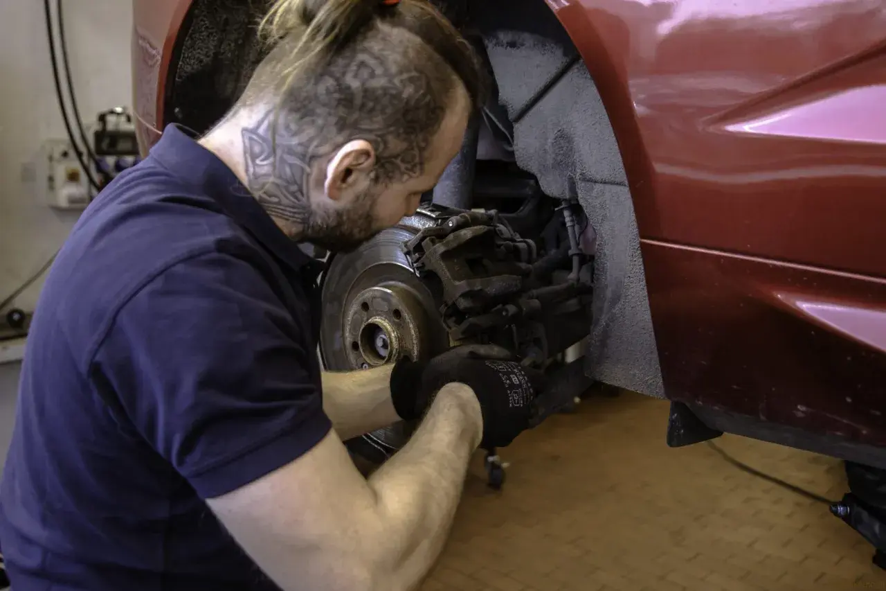 Mechanik w rękawiczkach naprawia hamulce w czerwonym Volvo. Dbałość o szczegóły zapewnia długą gwarancję.