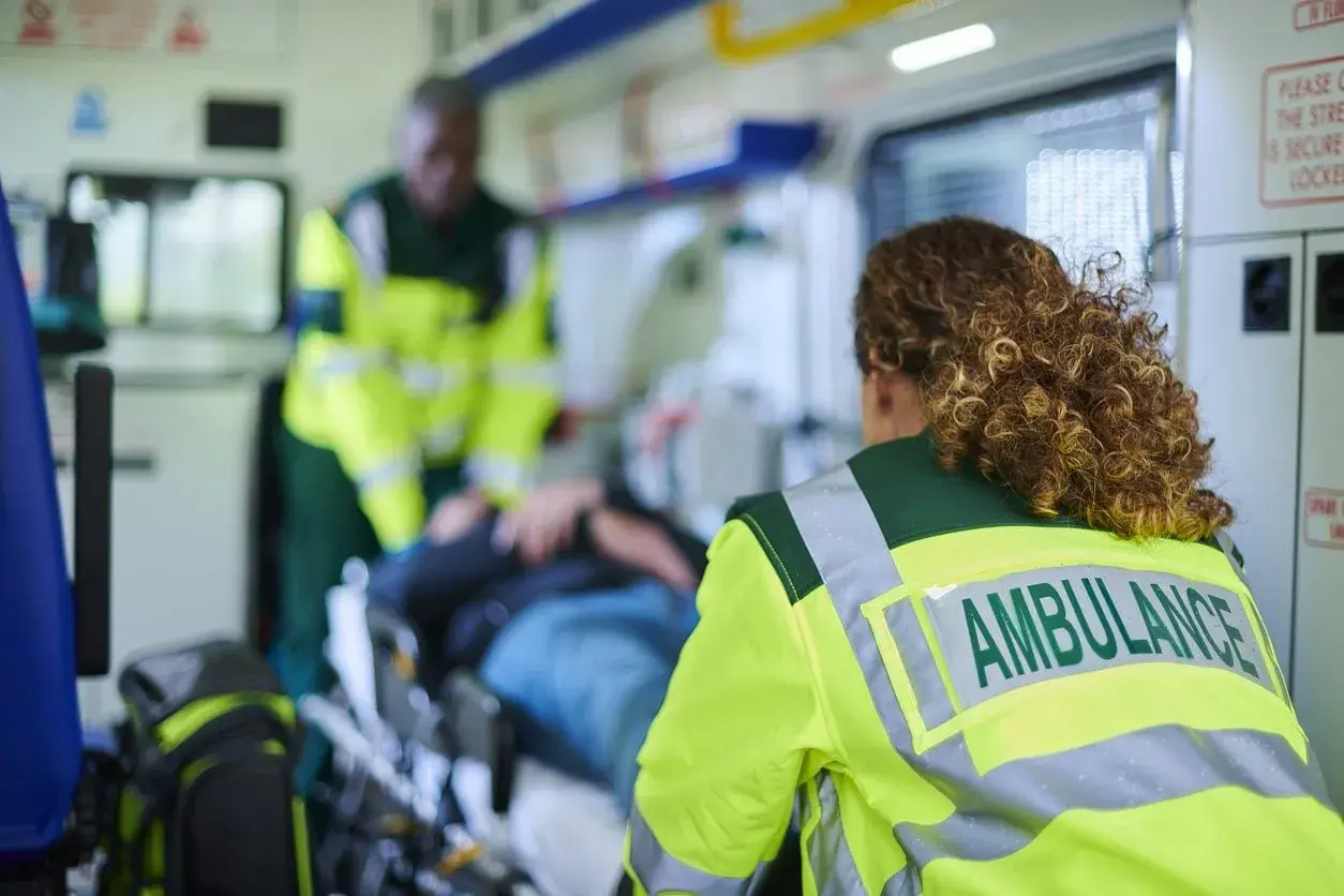 Personale sanitario assiste paziente su barella in ambulanza, garantendo il trasporto sicuro secondo la legge 104.