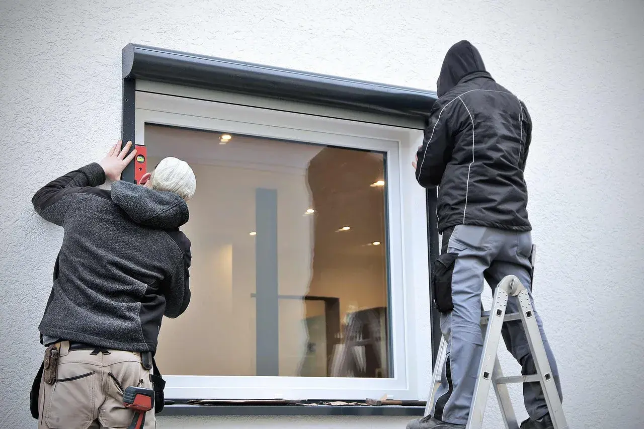 Zwei Handwerker führen die vorbaurollladen montage durch. Einer richtet mit Wasserwaage aus, der andere steht auf Leiter.