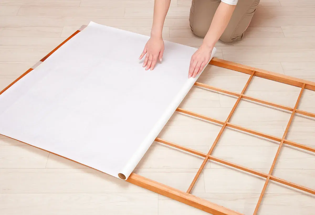 Mains déroulant du papier pour fabriquer une cloison japonaise sur un cadre en bois.