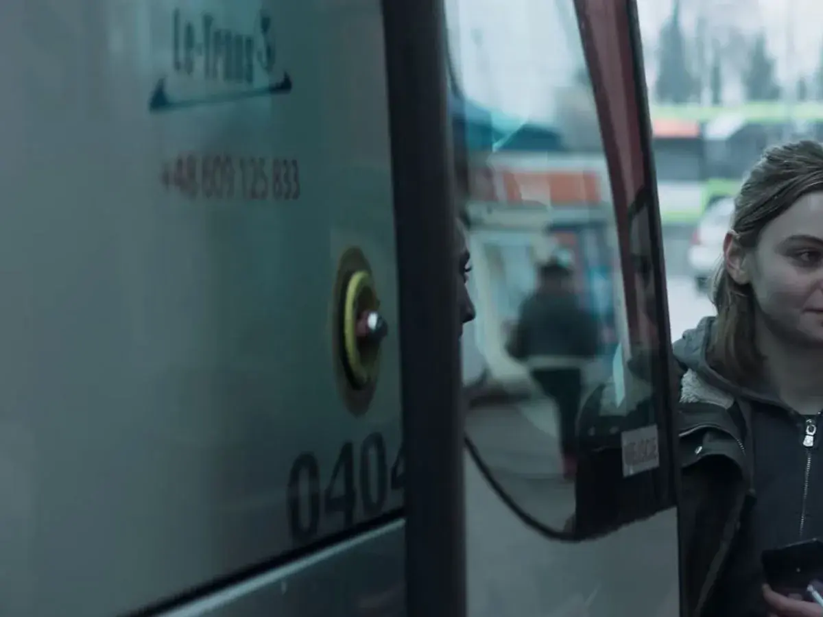Młoda kobieta patrzy w lustro autobusu, marząc, by jak najdalej stad.