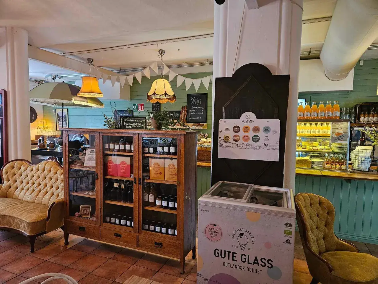 Mysigt café med en gul sammetssoffa, ett vitrinskåp fyllt med godsaker och en frys med "Gute Glass" Gotländsk godhet.