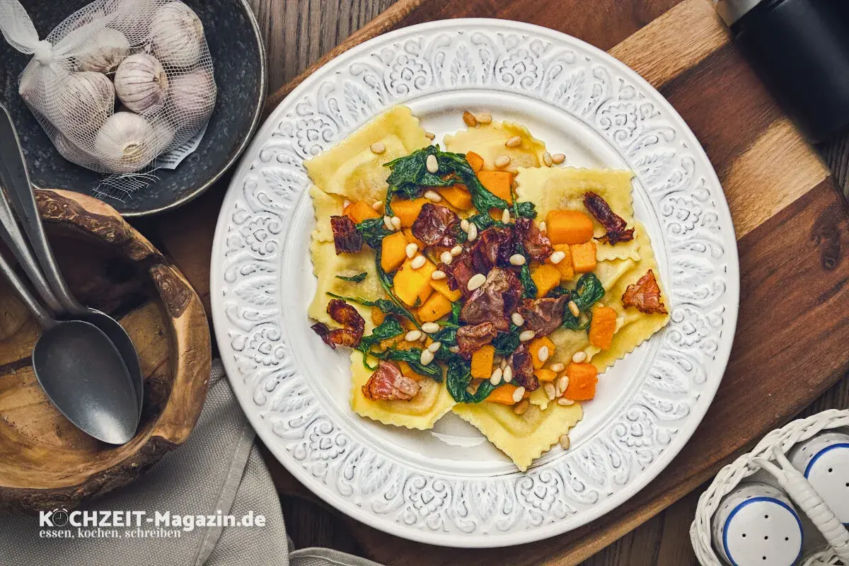 Ravioli mit Kürbis, Spinat und Pinienkernen – ein köstliches ravioli rezept. Daneben Knoblauch und Löffel.