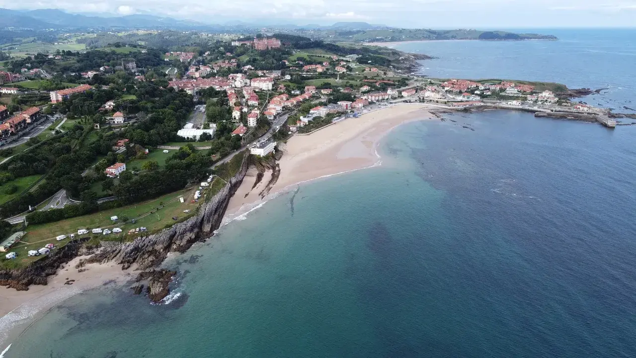 Vista aérea de la **playa de Comillas**, con sus casas, acantilados y el mar Cantábrico.