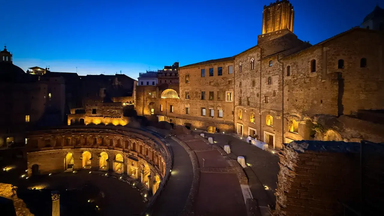 Il mercato di Traiano illuminato di notte, con le sue antiche mura di mattoni e l'arco semicircolare, evoca un'atmosfera magica.