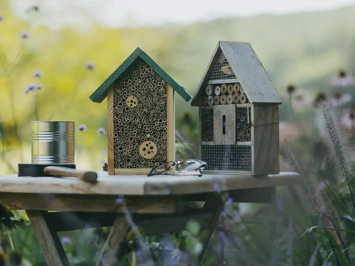Zwei selbstgebaute Insektenhotels stehen auf einem Tisch im Garten. Ein Insektenhotel bauen ist eine tolle Idee für jeden Naturliebhaber.
