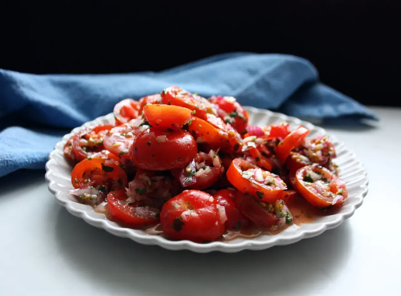En härlig tomat sallad med rödlök och örter, serverad på en vit, mönstrad tallrik.