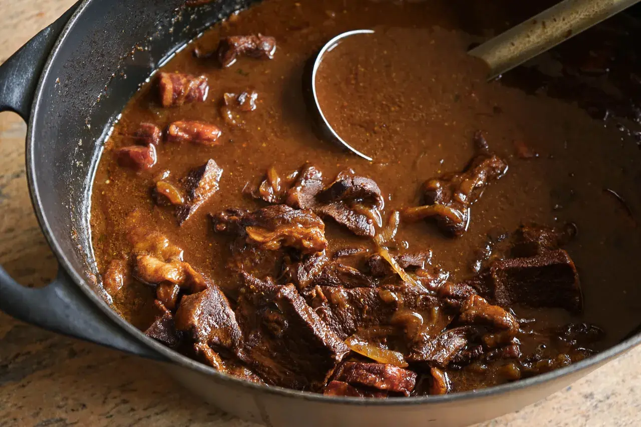 Un plat mijoté de carbonade flamande dans une cocotte en fonte, avec des morceaux de bœuf tendres et une sauce brune onctueuse.