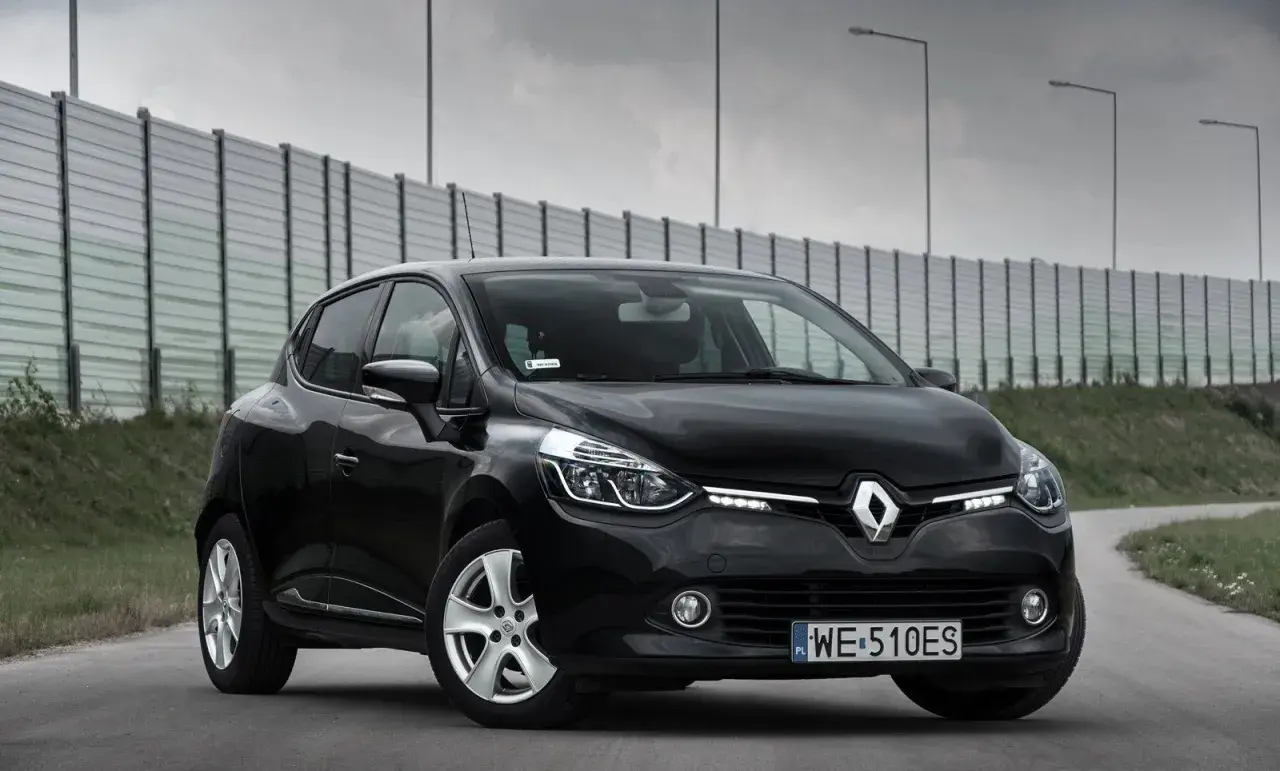 Czarny Renault Clio 4 z 2013 roku na drodze, z barierą dźwiękochłonną w tle.