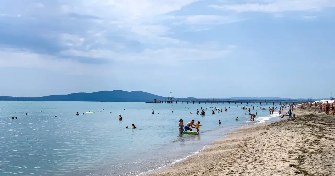Plaża w Burgas, mnóstwo ludzi kąpiących się i opalających. Długie molo, góry w tle. Burgas czy warto? Zdecydowanie tak!
