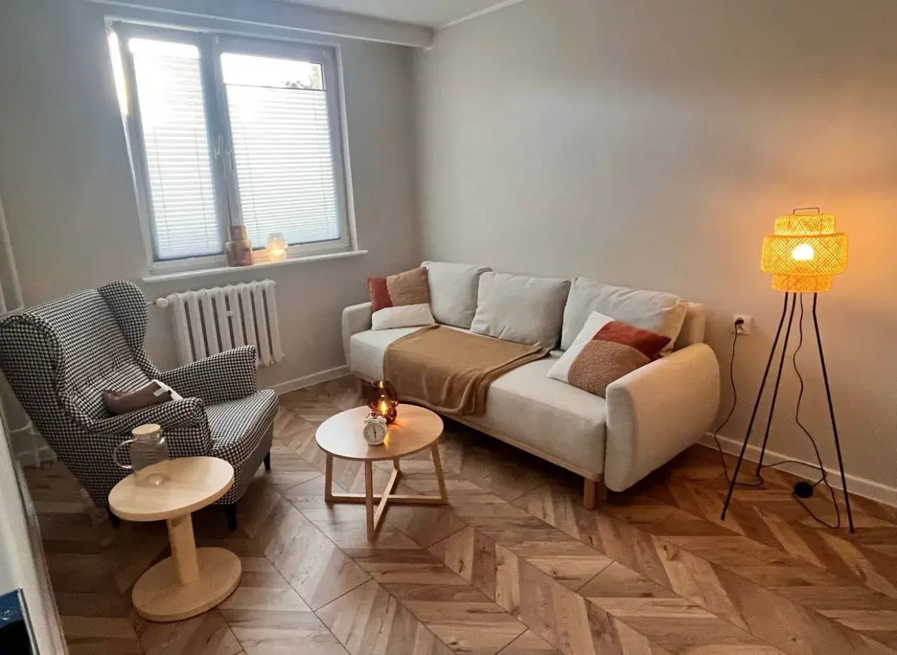 Przytulny gabinet terapeutyczny z sofą, fotelem i lampą.