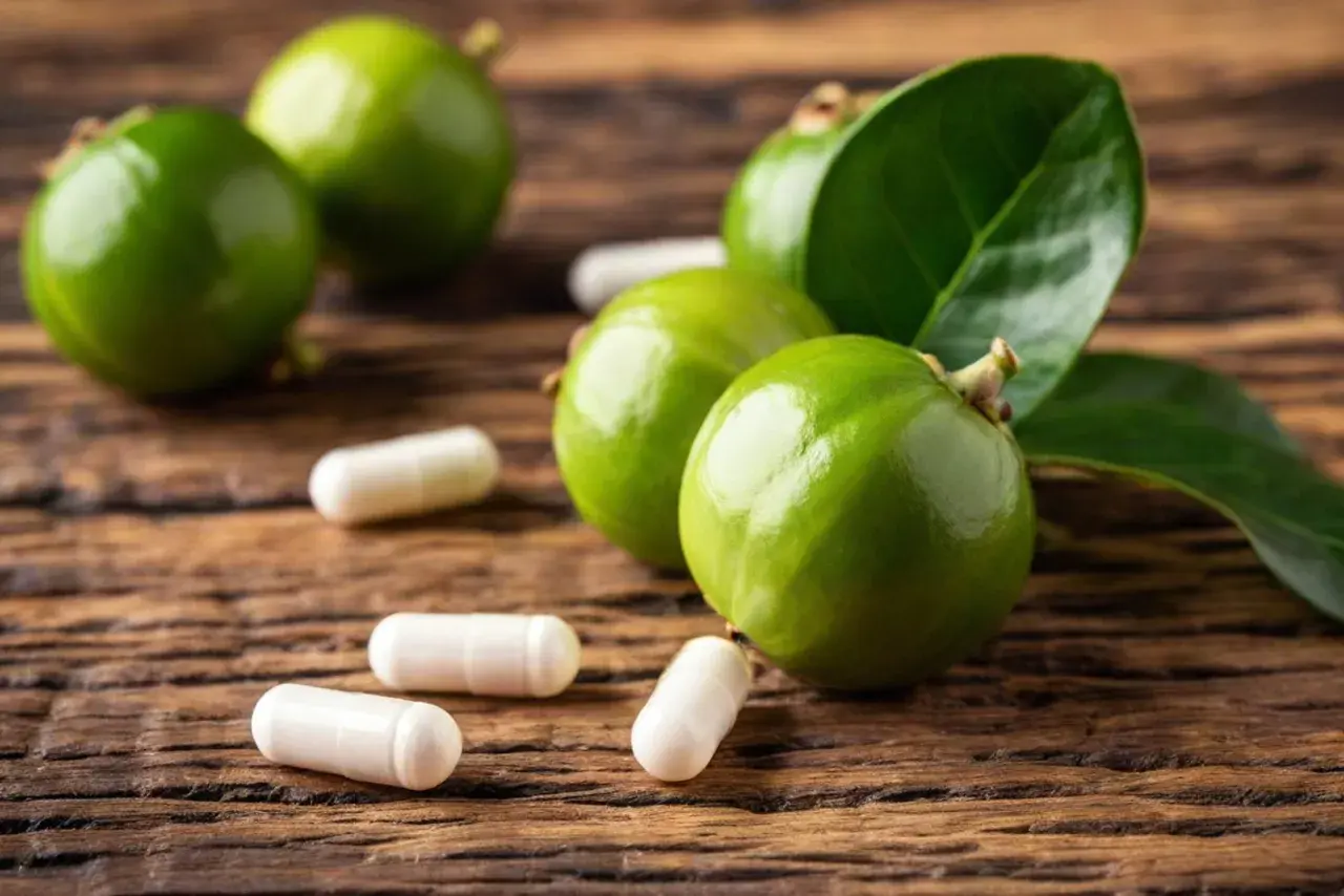 Frutti verdi di garcinia cambogia e capsule su legno.