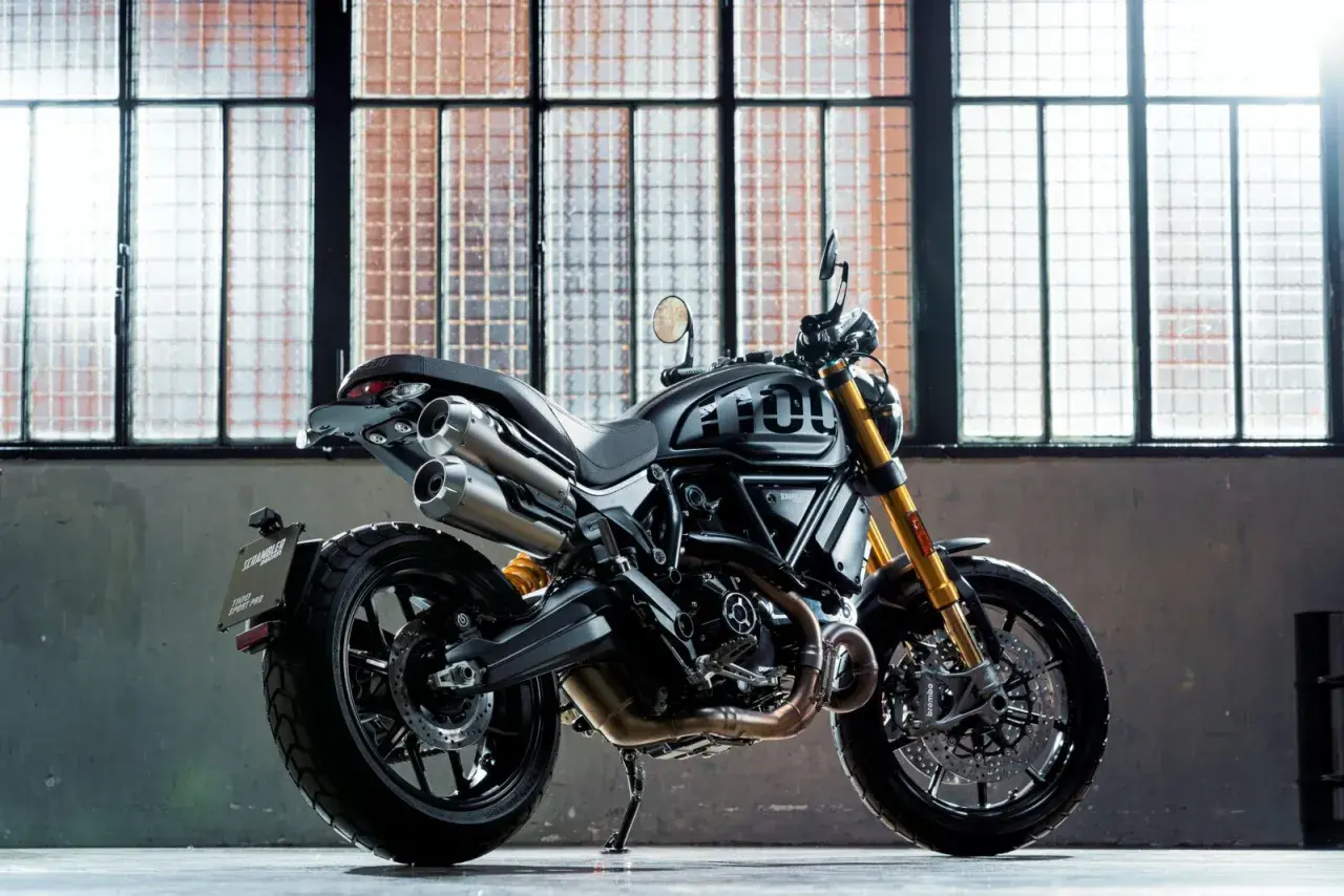 Czarny motocykl Ducati Scrambler 1100 Sport Pro, jeden z najlepszych motocykli, stoi przed industrialnymi oknami.