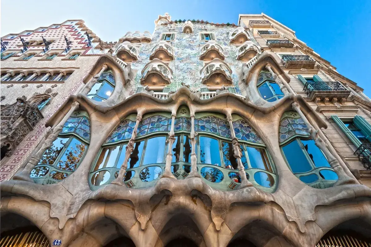 Façade d'un bâtiment à l'architecture organique, avec un **art nouveau motif végétal** sculpté dans la pierre et des vitraux bleus.