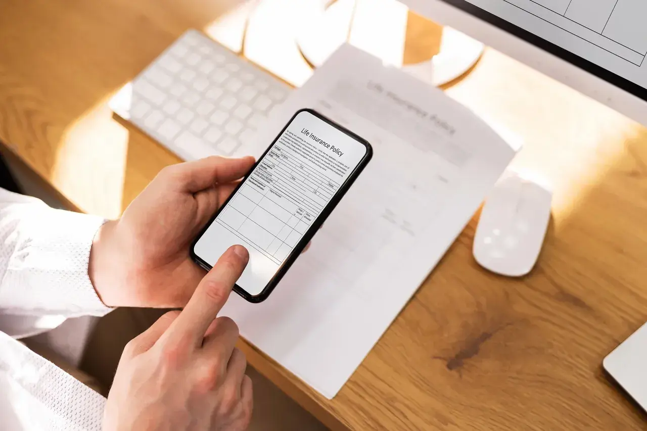 Dłoń trzyma smartfon, który działa jak darmowy skaner dokumentów, skanując polisę ubezpieczeniową.