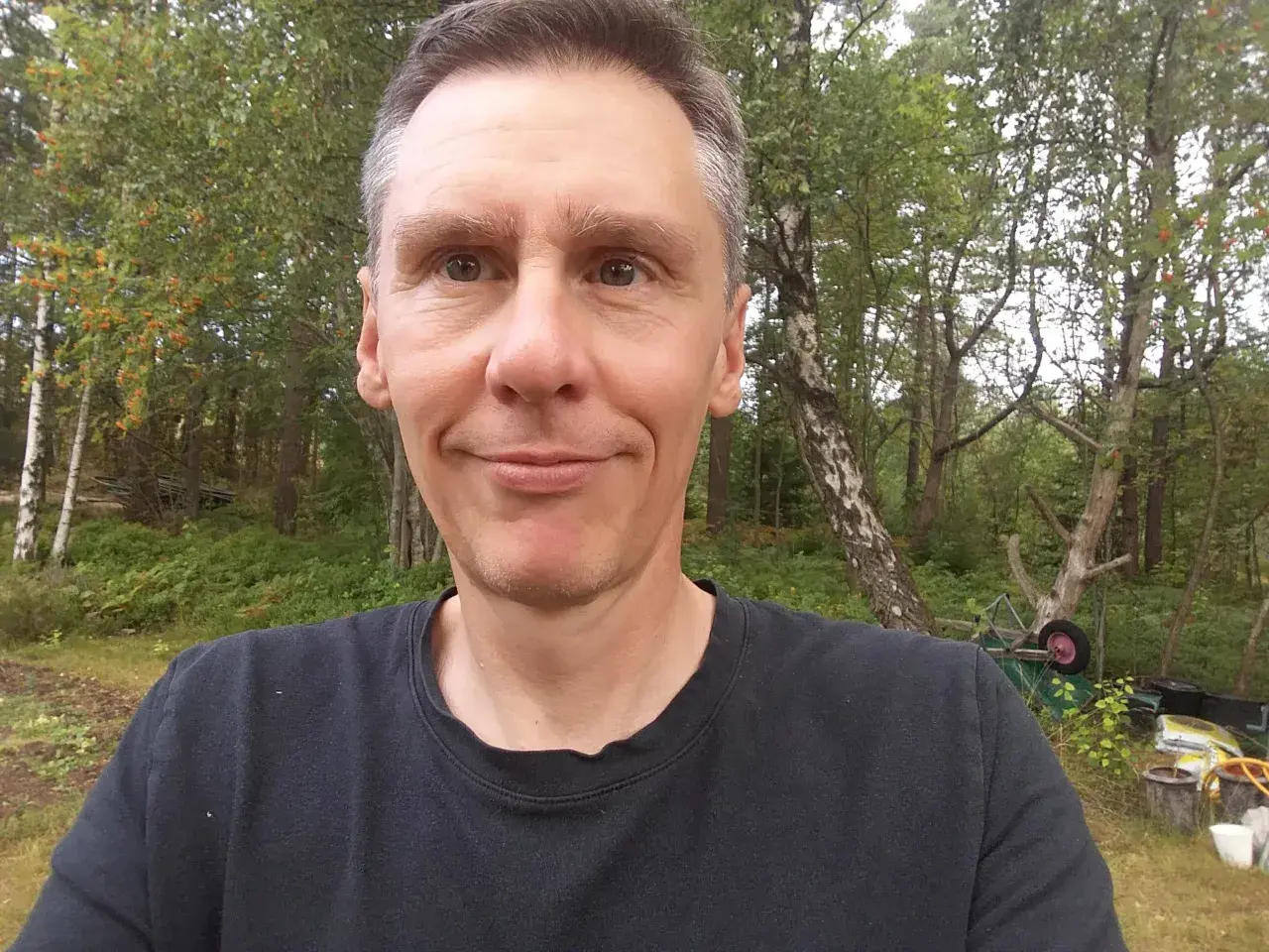 Johan Nilsson ler mot kameran i en skogsmiljö med träd och buskar.