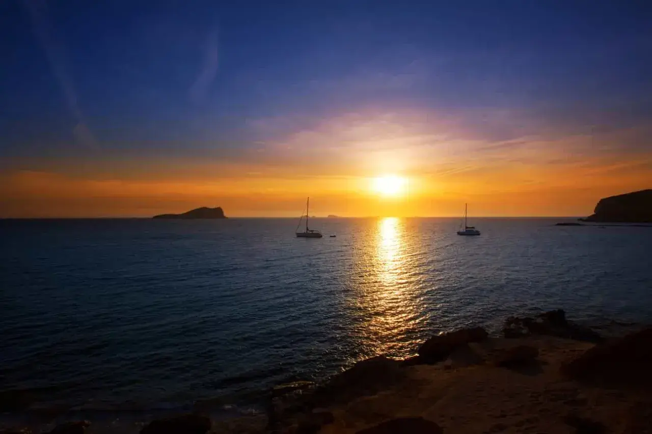 Un atardecer mágico en Ibiza, con veleros navegando y el sol tiñendo el mar de oro. Un lugar perfecto donde ver el atardecer en Ibiza.