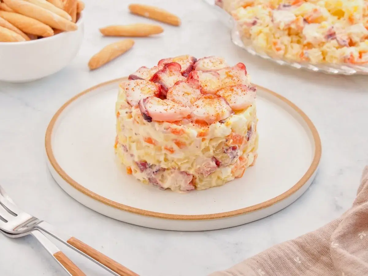 Deliciosa ensaladilla de pulpo, con patatas, zanahoria y huevo, coronada con trozos de pulpo y pimentón.