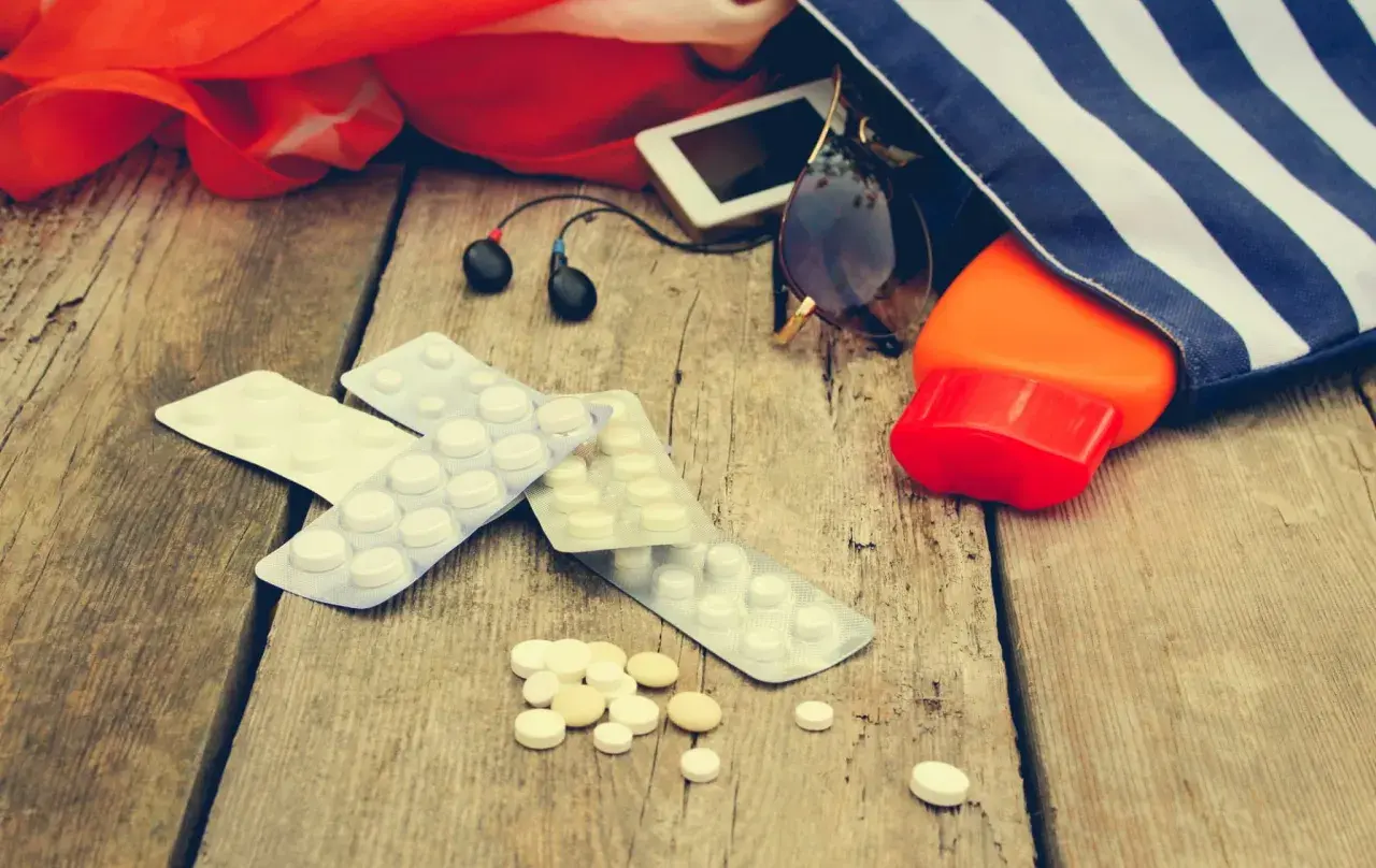 Medikamente gegen Kreislaufprobleme bei Hitze liegen neben Sonnencreme, Sonnenbrille und Kopfhörern auf Holz.