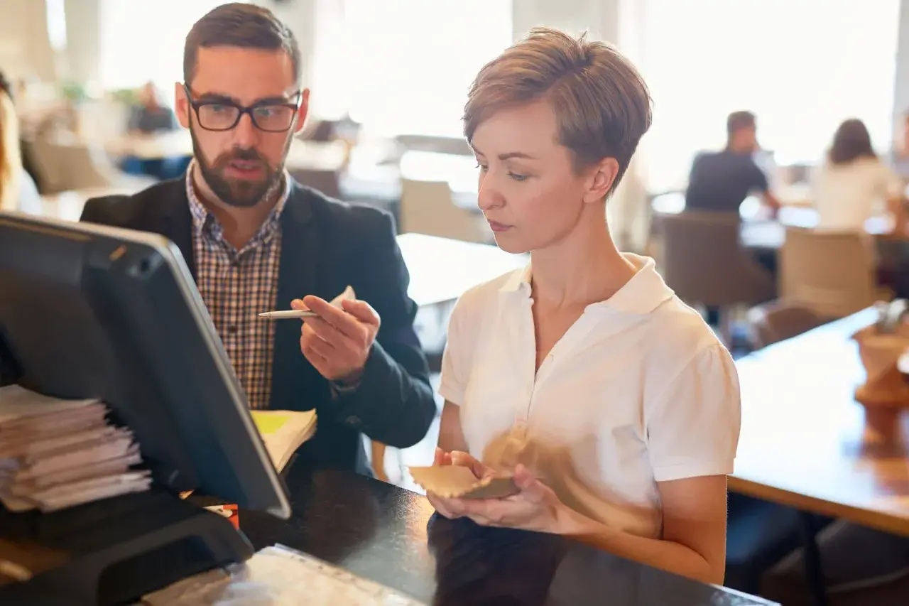 Mann mit Brille und Frau besprechen etwas am Kassensystem in einem Restaurant.