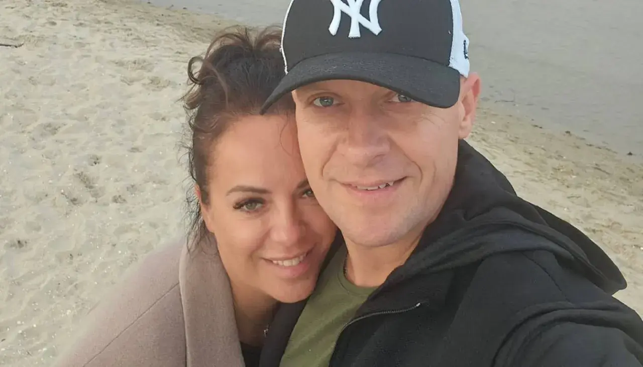 Piotr Marciniak z żoną na plaży, uśmiechnięci i blisko siebie.