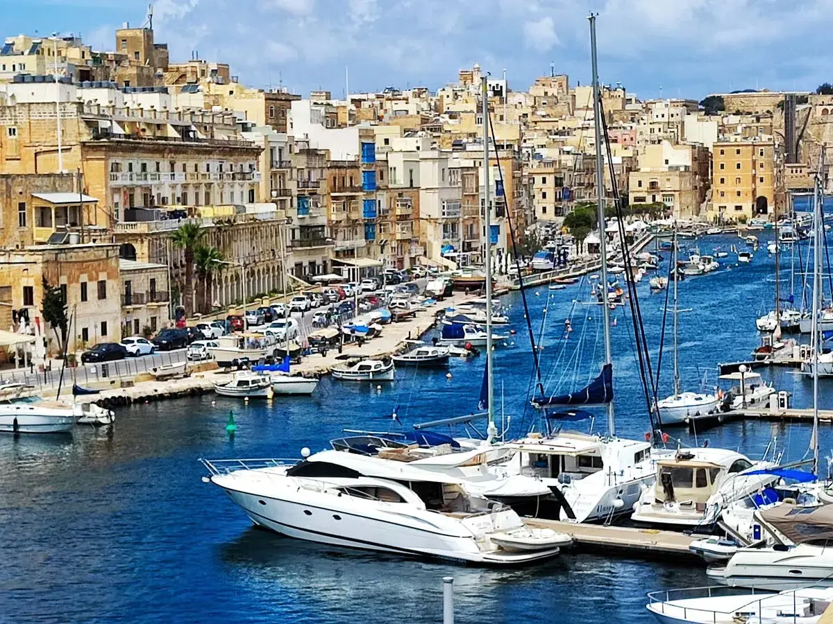 Malta historia: malowniczy port pełen jachtów, z zabytkową zabudową w tle.