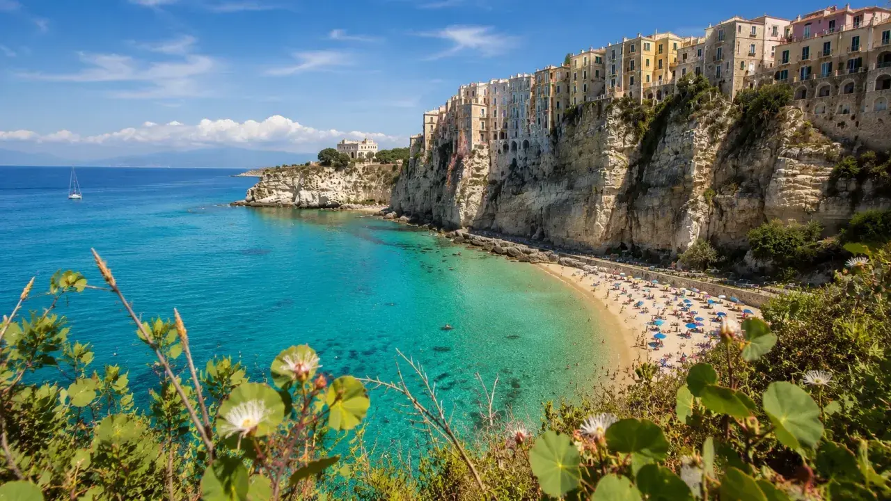 A vibrant beach scene on the Calabria coast, with colorful buildings perched on dramatic cliffs overlooking turquoise waters.