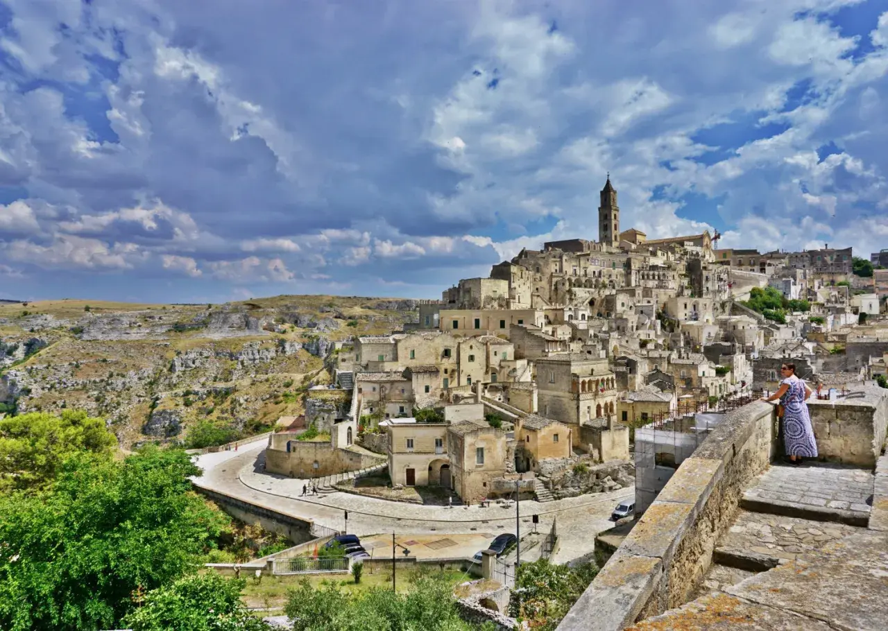 A woman in a patterned dress surveys the ancient Sassi di Matera, Italy. This view offers a glimpse of what to do in Matera Italy: explore its unique cave dwellings and historic architecture.